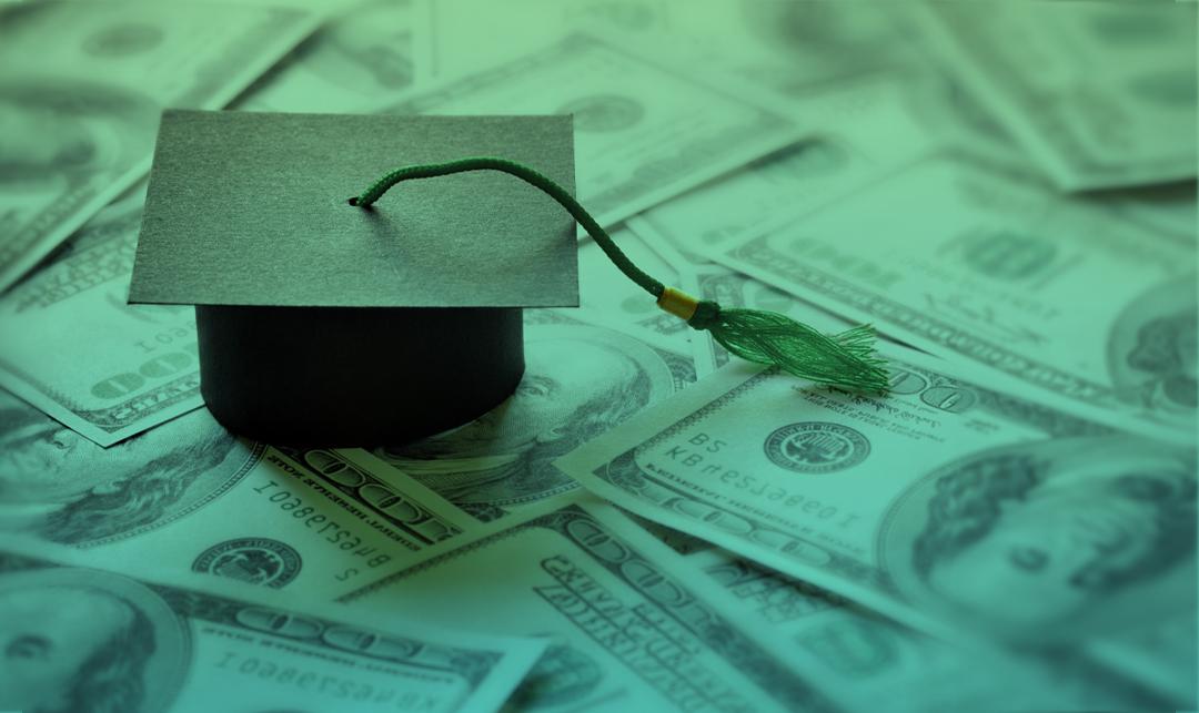 graduation cap on background of hundred dollar bills